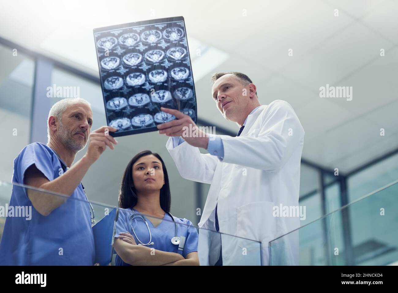 Examining the patients latest scans. Shot of a group of doctors looking at a medical scan while standing in a hospital. Stock Photo
