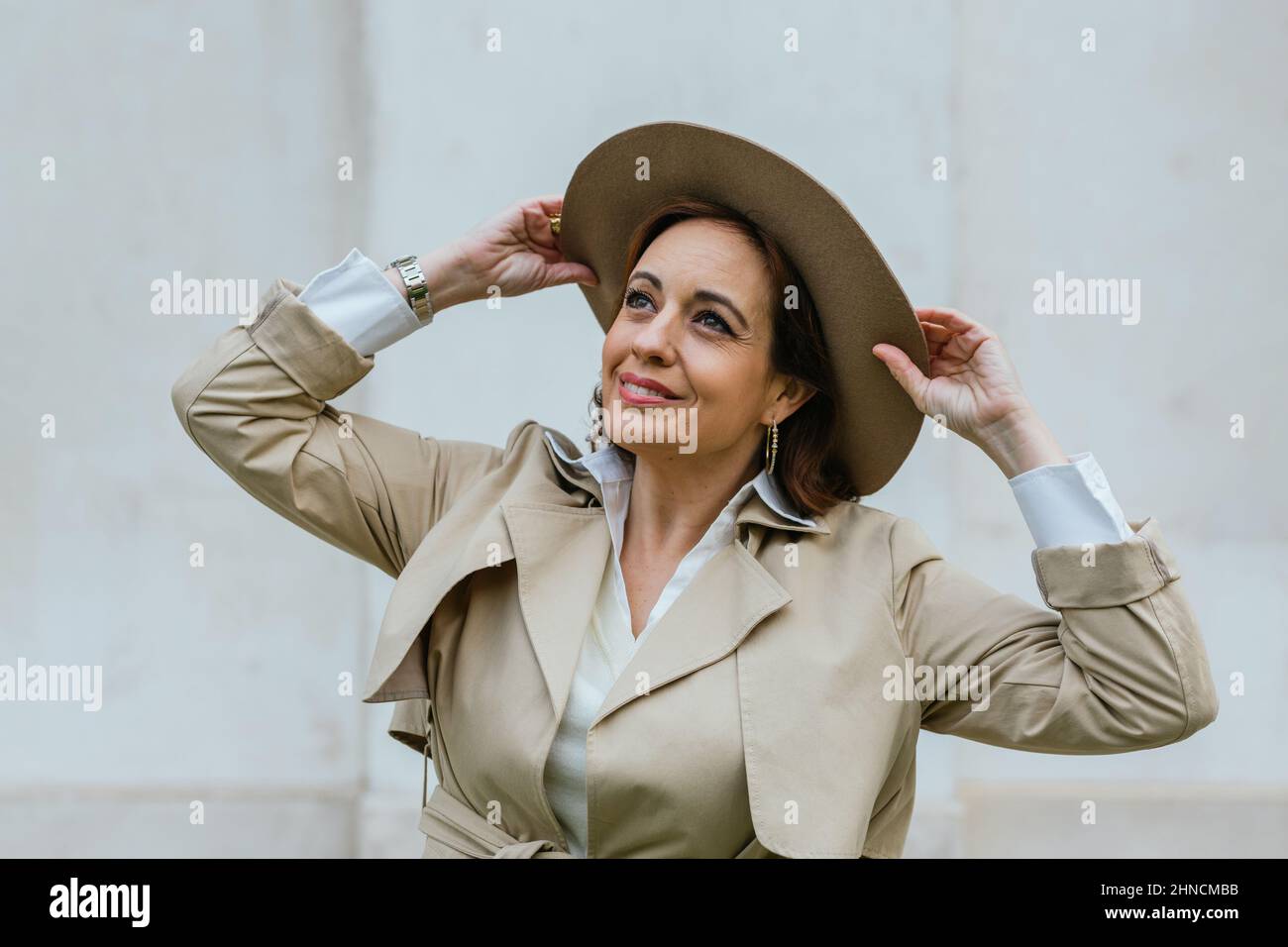 Smiling woman in trench coat and hat while standing outdoors on the ...