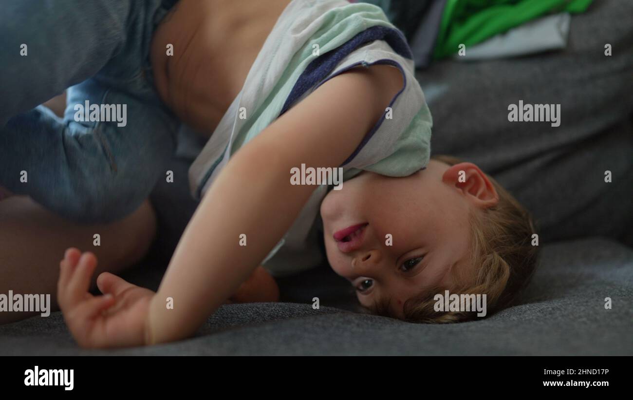 Bored little boy at home in upside down on sofa child playing alone ...