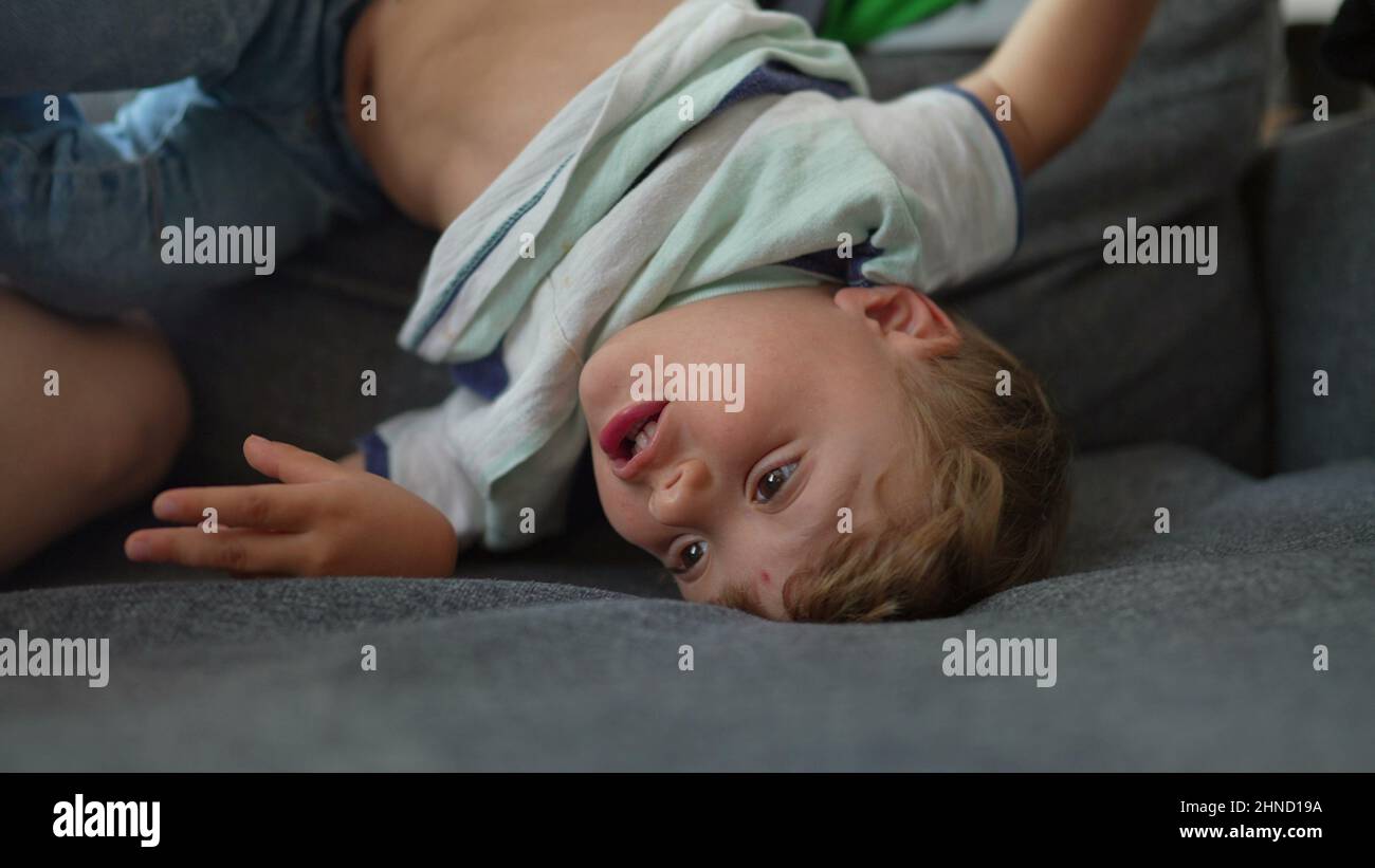 Bored little boy at home in upside down on sofa child playing alone ...