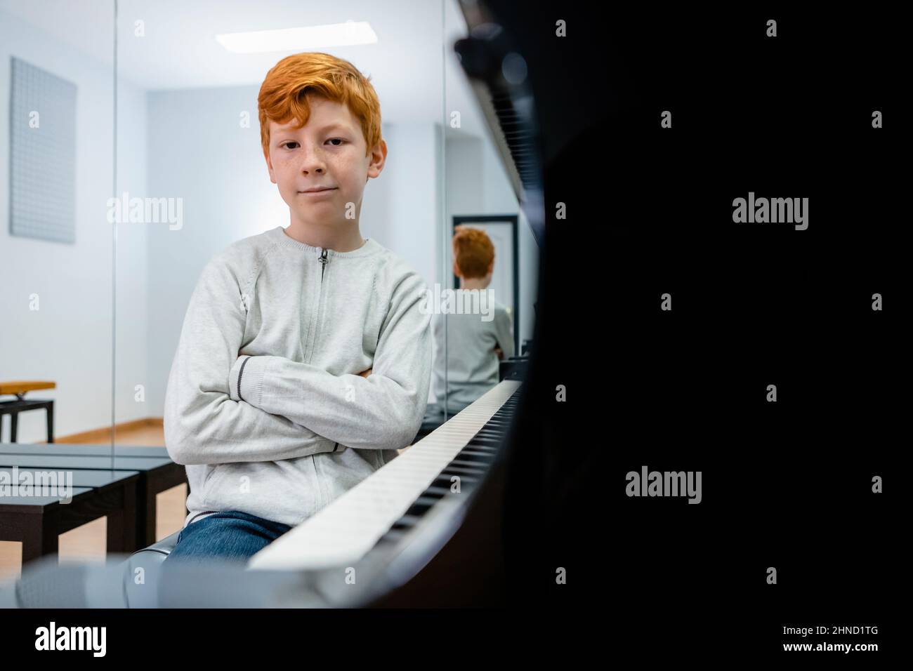 Content ginger preteen child sitting near piano in classroom and looking at camera Stock Photo