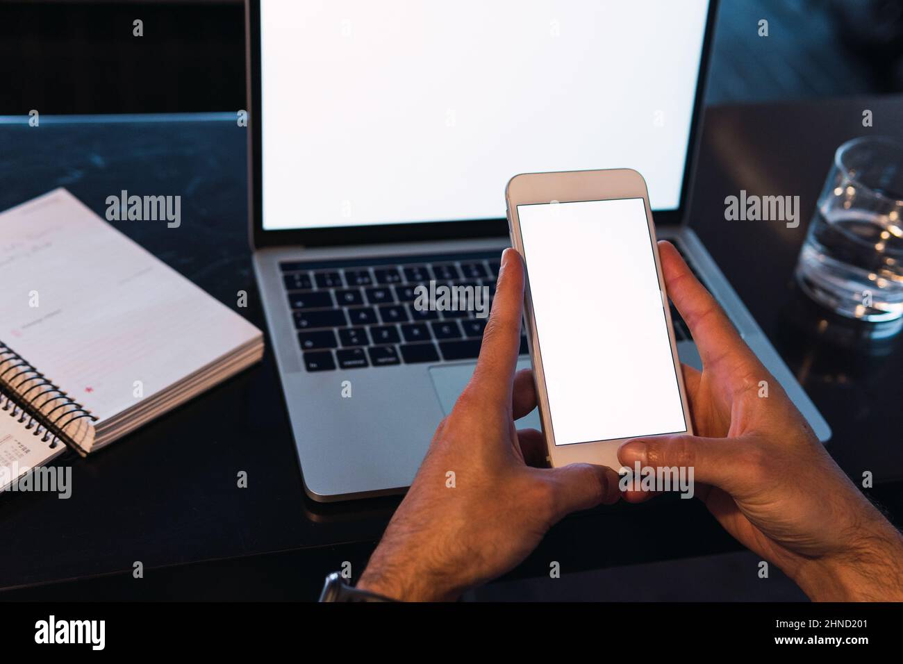 From above of crop unrecognizable male worker text messaging on cellphone with empty screen while sitting at table with netbook Stock Photo