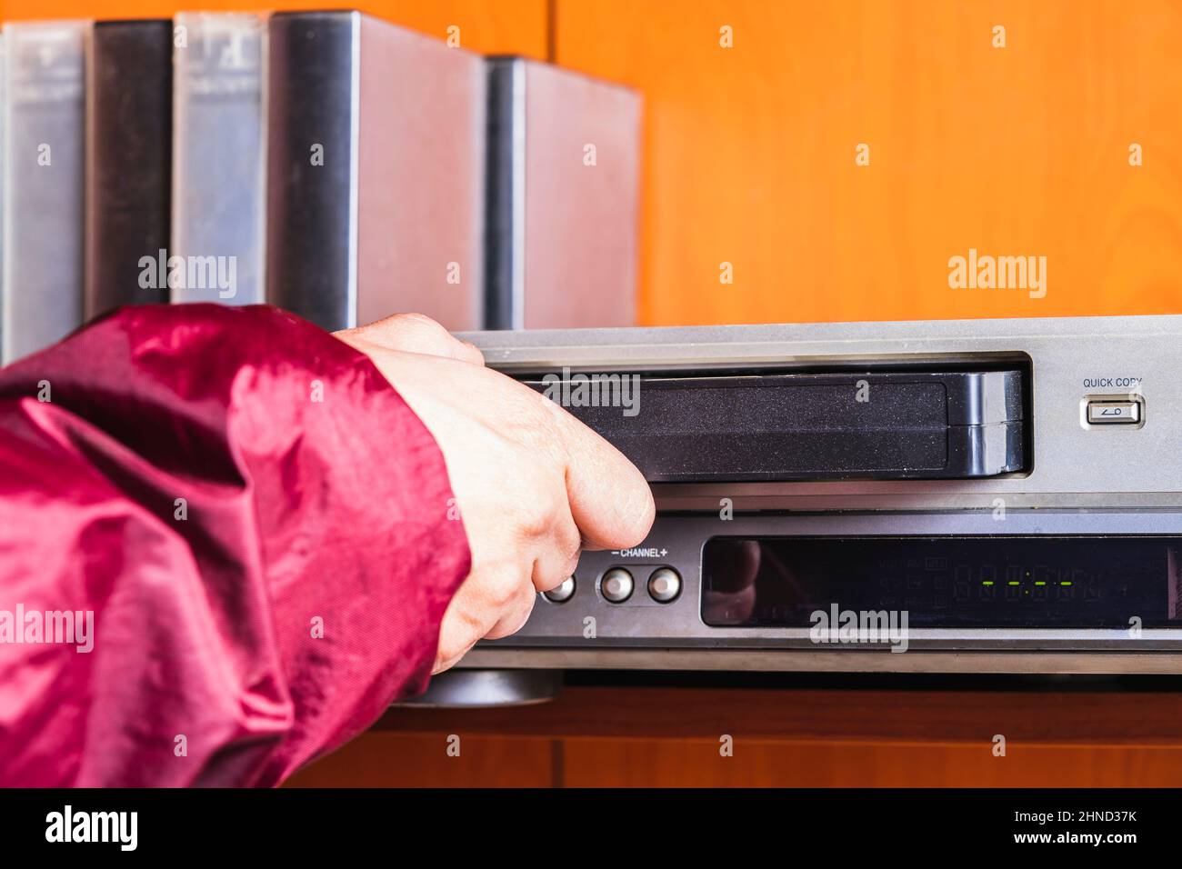 Person putting a VHS tape into the player wearing a retro 90's jacket