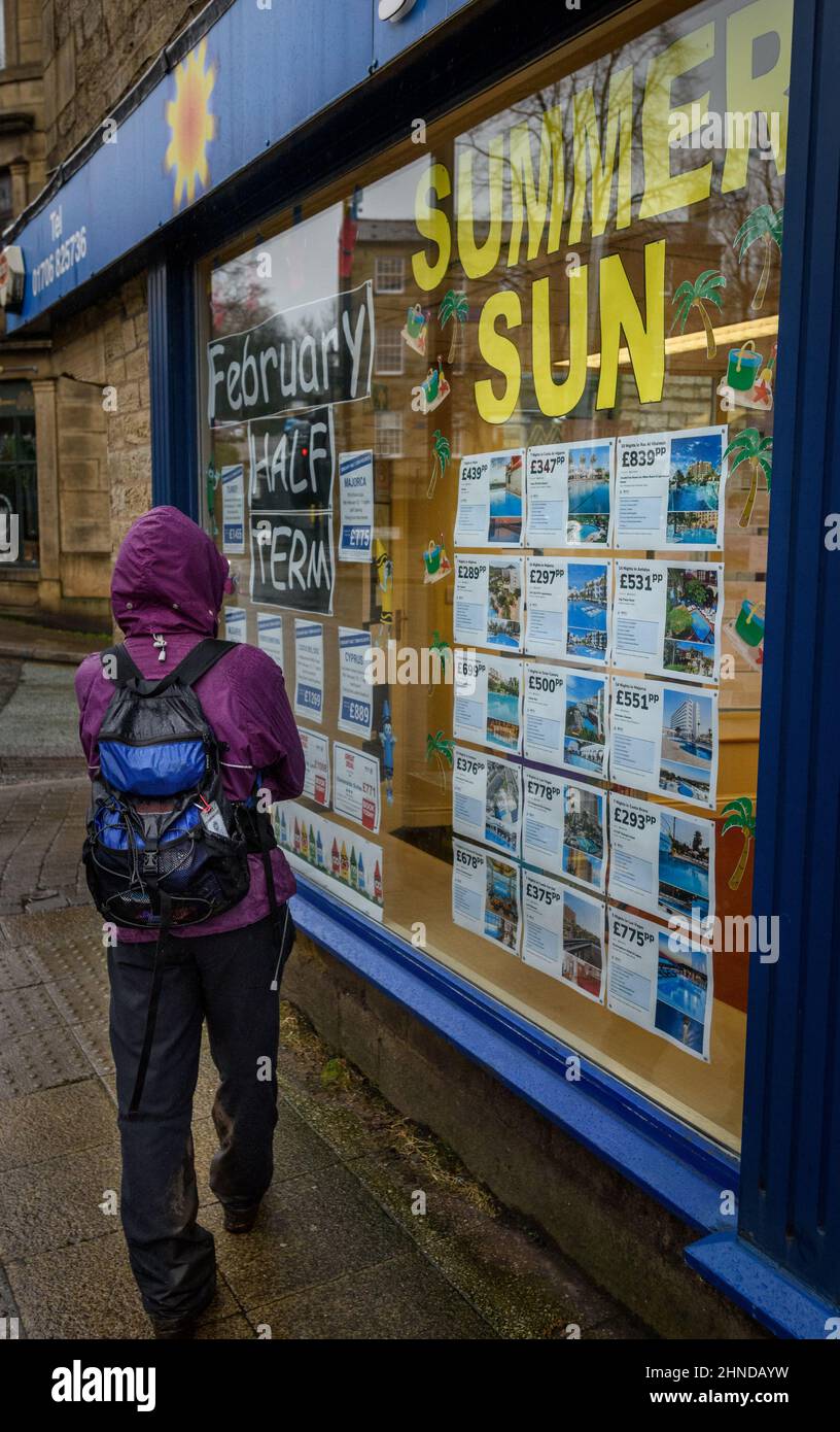 Ramsbottom, Lancashire, UK, Wednesday February 16, 2022. The start of Storm Dudley hits the North West of England on Bridge Street, Ramsbottom, Lancashire. A shopper stops to check out the summer sun offers outside this travel agent. Credit: Paul Heyes/Alamy News Live Stock Photo