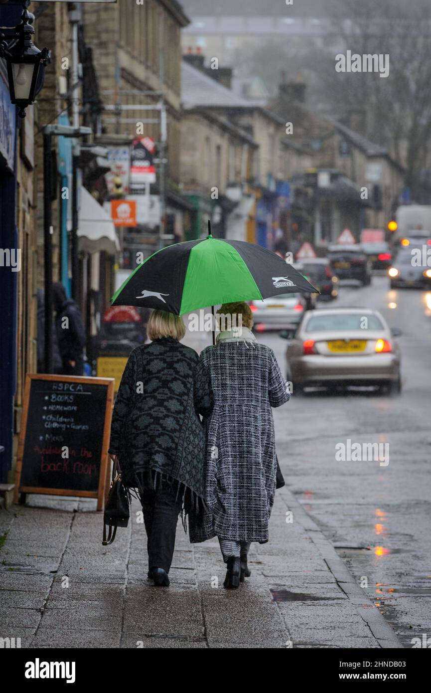 Ramsbottom, Lancashire, UK, Wednesday February 16, 2022. The start of Storm Dudley hits the North West of England on Bridge Street, Ramsbottom, Lancashire. Shppers take shelter under an umbrella as the rain starts to fall. Credit: Paul Heyes/Alamy News Live Stock Photo