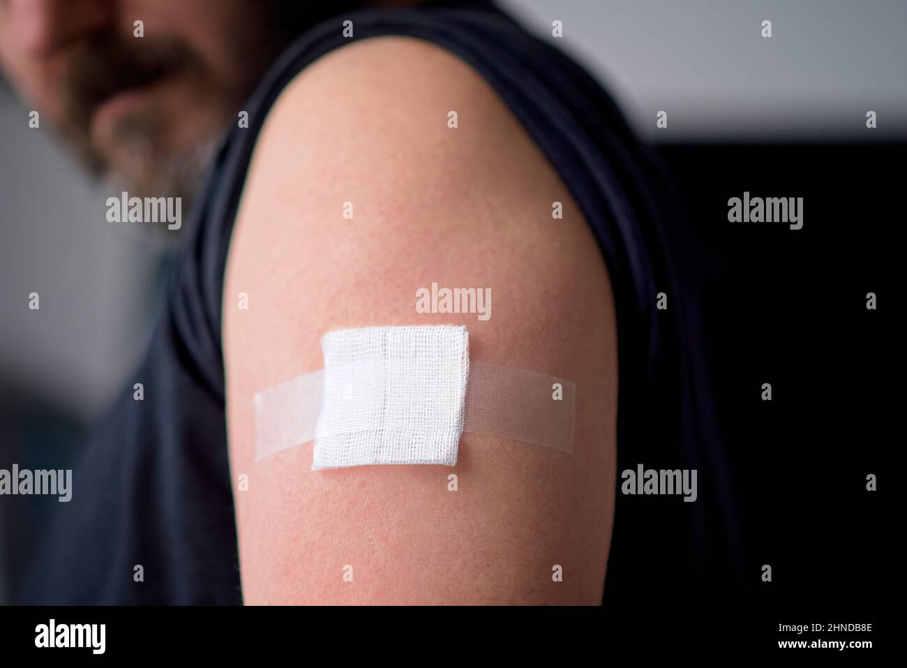 Vaccinated man looking down at plaster bandage on shoulder right after getting covid-19 vaccine shot. Booster shot concept. High quality photo Stock Photo
