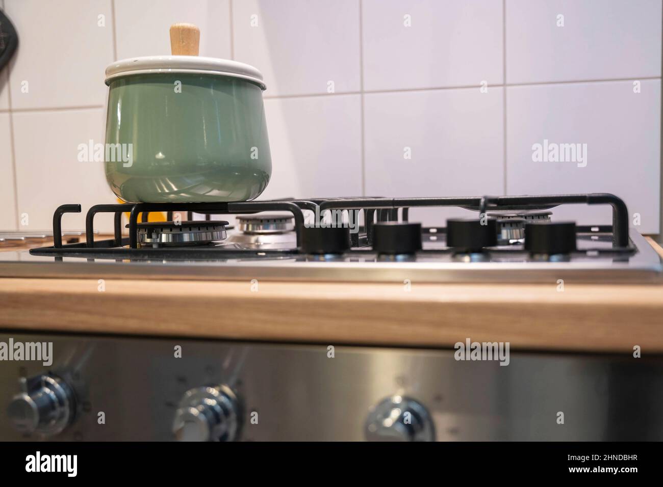 a light green saucepan with a lid stands on a home gas stove, home cooking, home kitchen interior Stock Photo