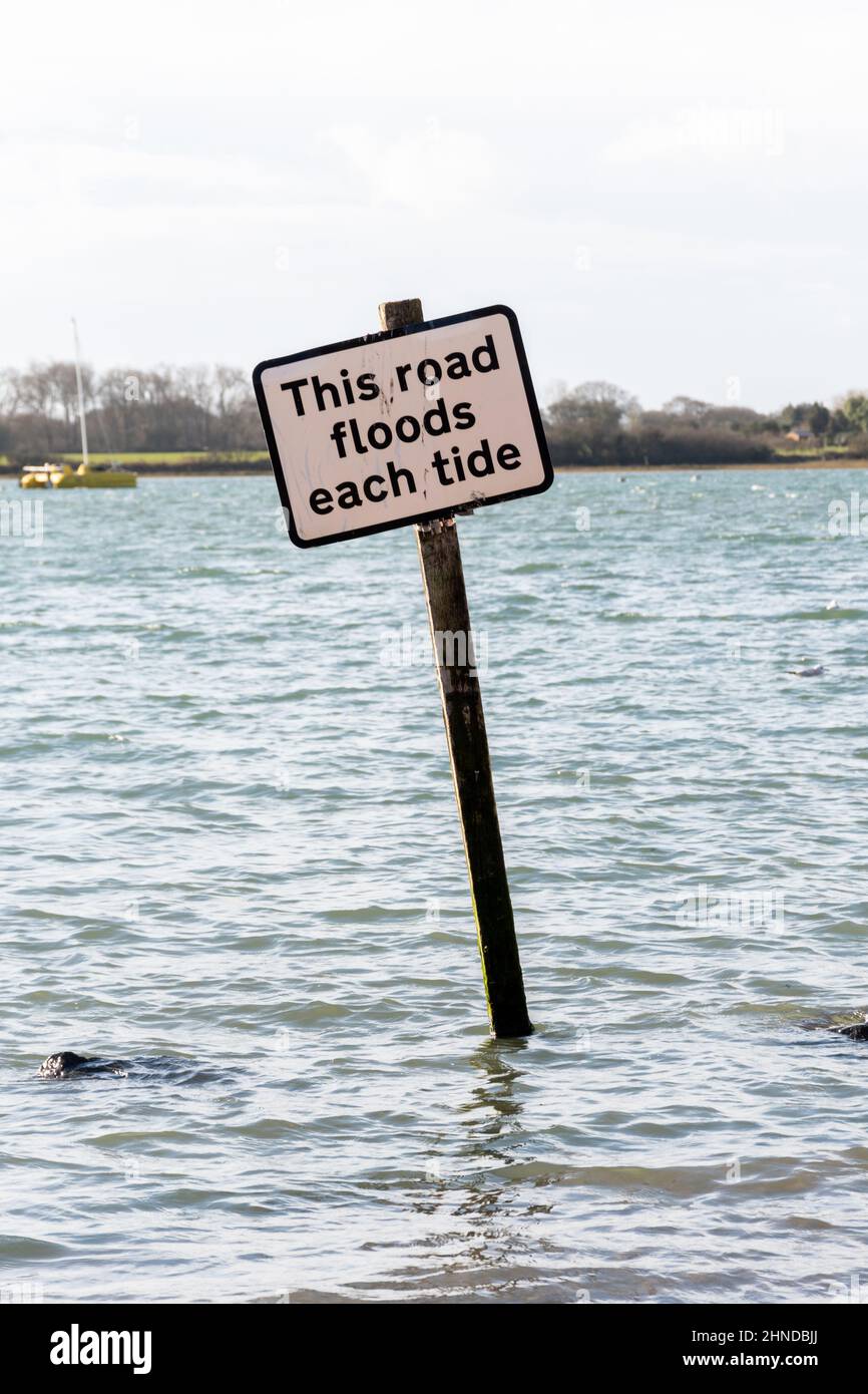 Sign reading This road floods each tide, in the sea at Bosham village, West Sussex, UK. The tidal Shore Road underwater at high tide. Stock Photo