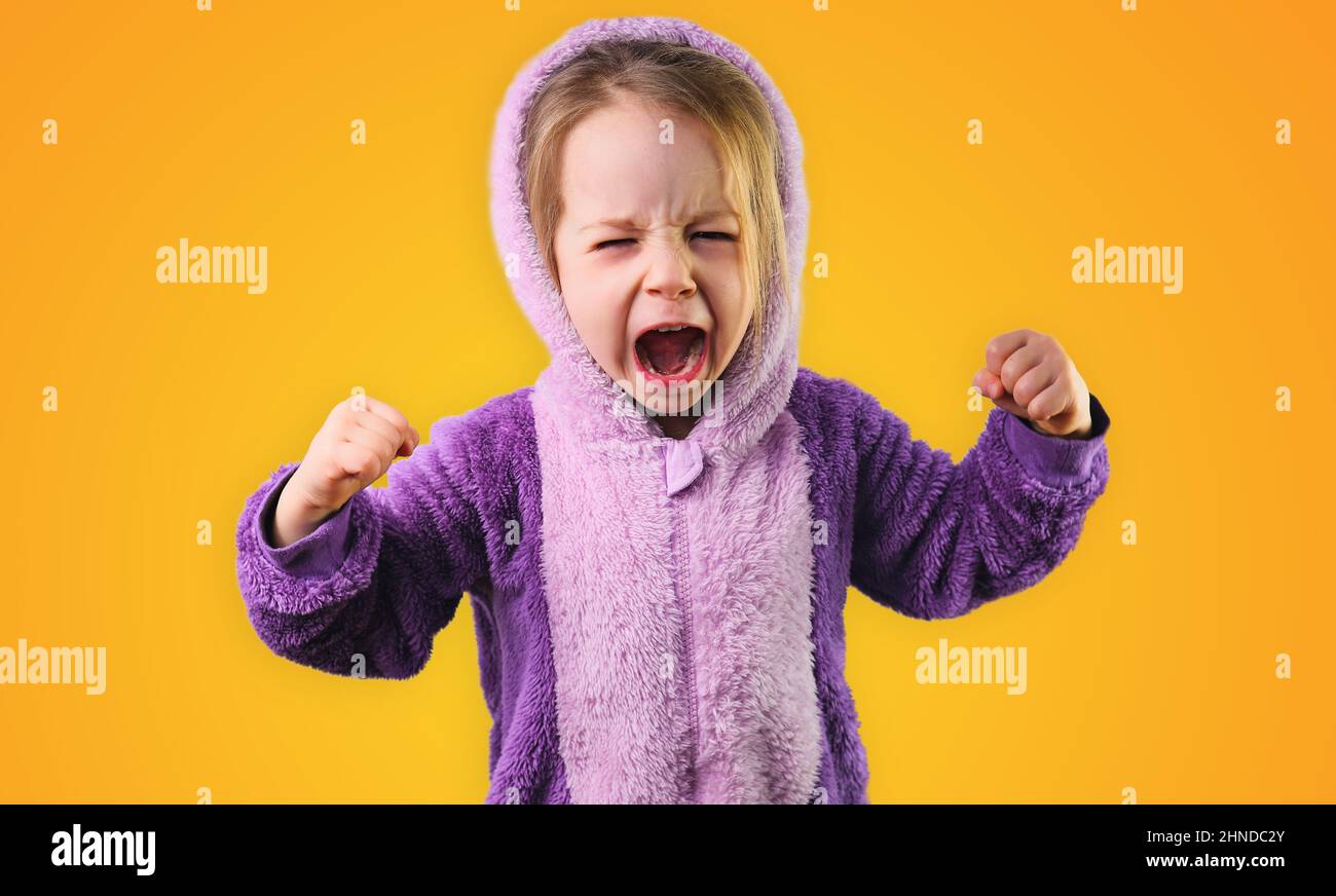 angry little toddler girl furiously screaming raise hands in purple pajamas Stock Photo