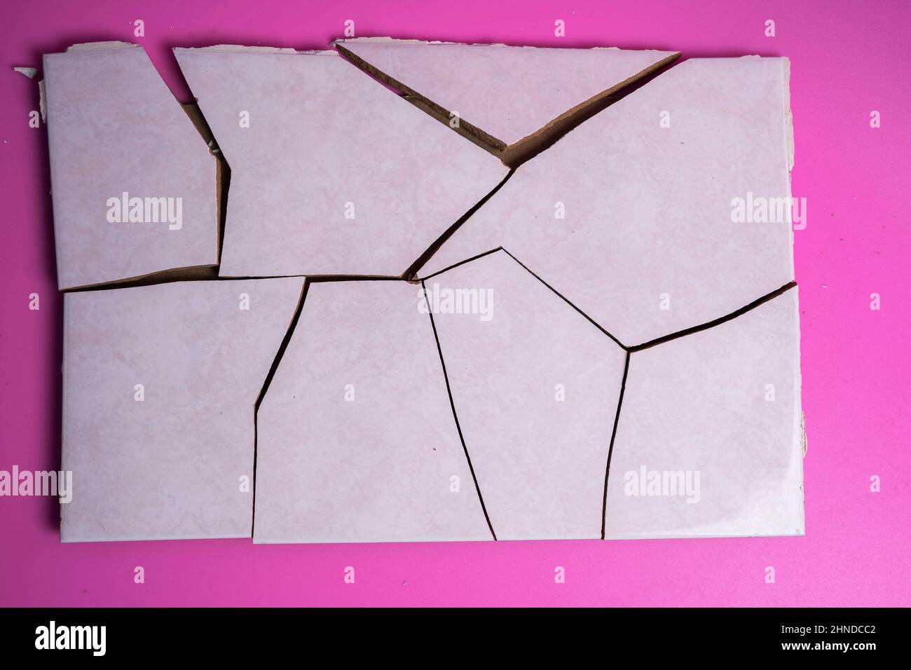 Cracked ceramic tile, broken into pieces on a pink background, tile