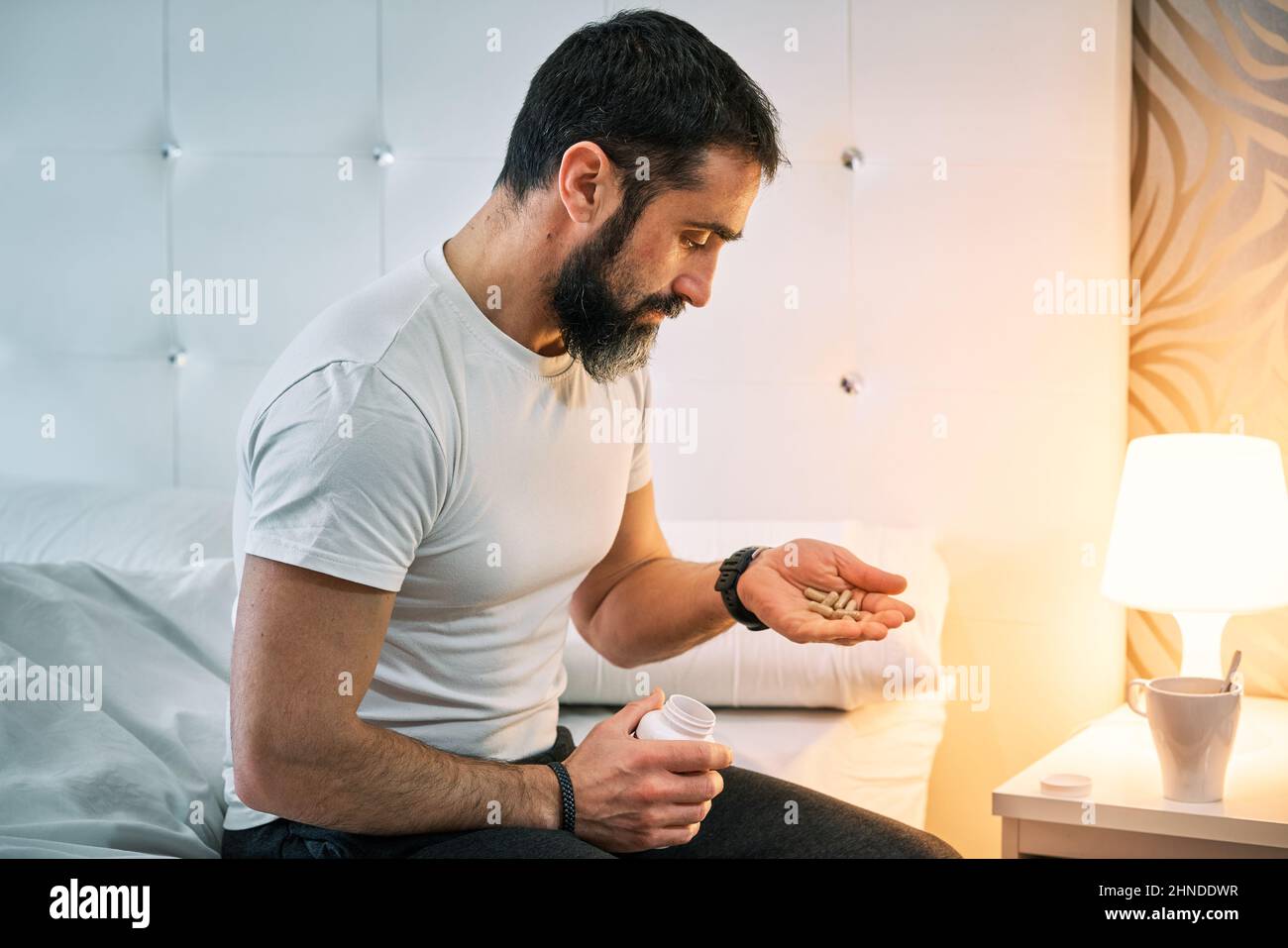 person with some kind of problem sitting on the bed and looking for a pill Stock Photo