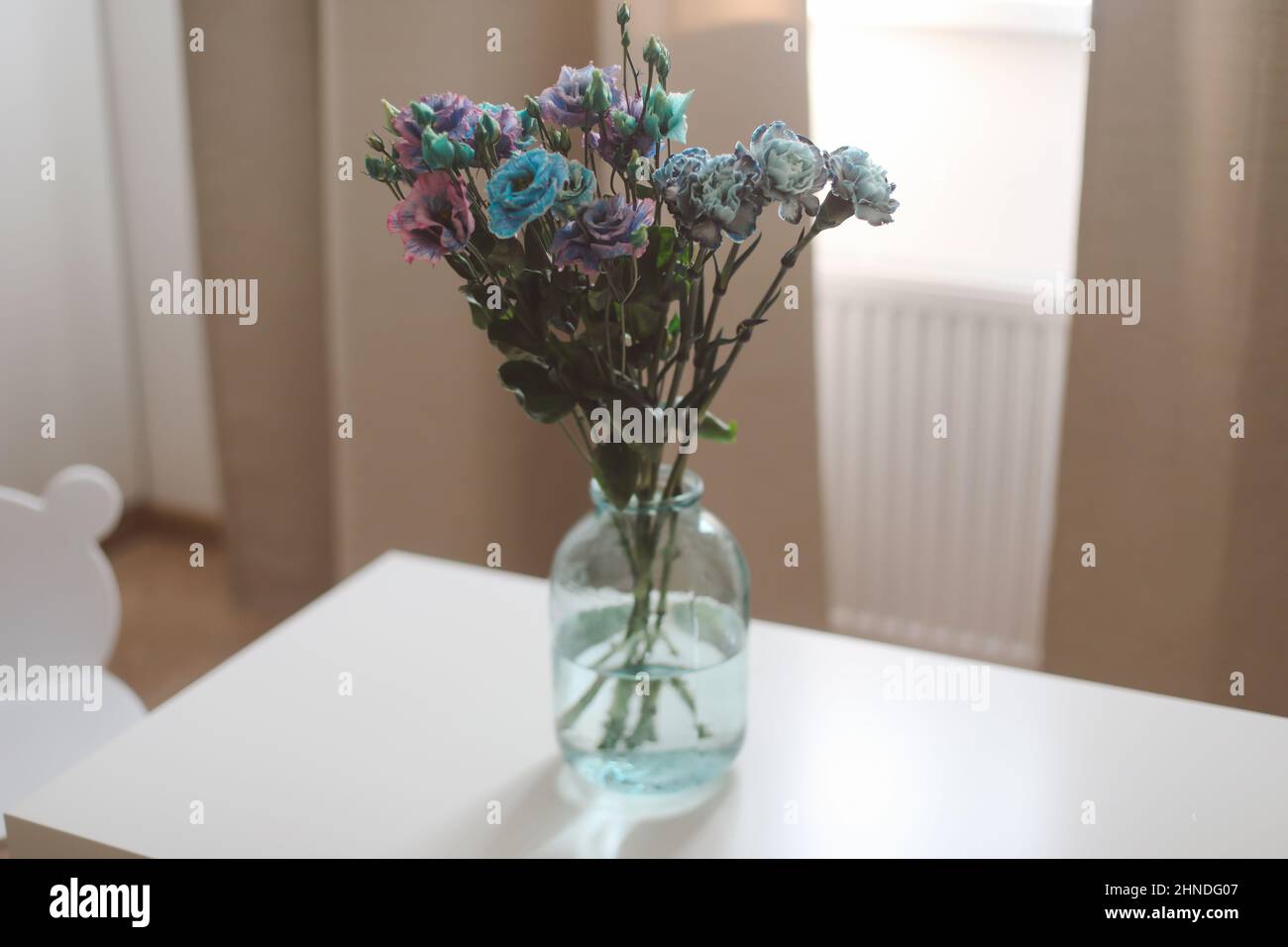 bunch of blue and purple flowers in a jar on the table in a sunny room, minimal home decor. Stock Photo