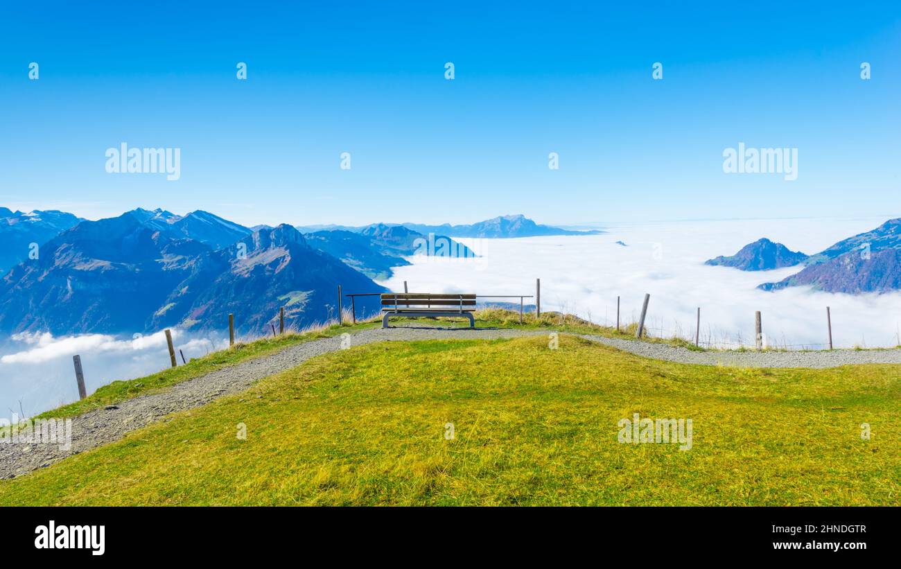 Bench on top of the mountain. Grandiose panorama of mountains and clouds from the top. Stock Photo