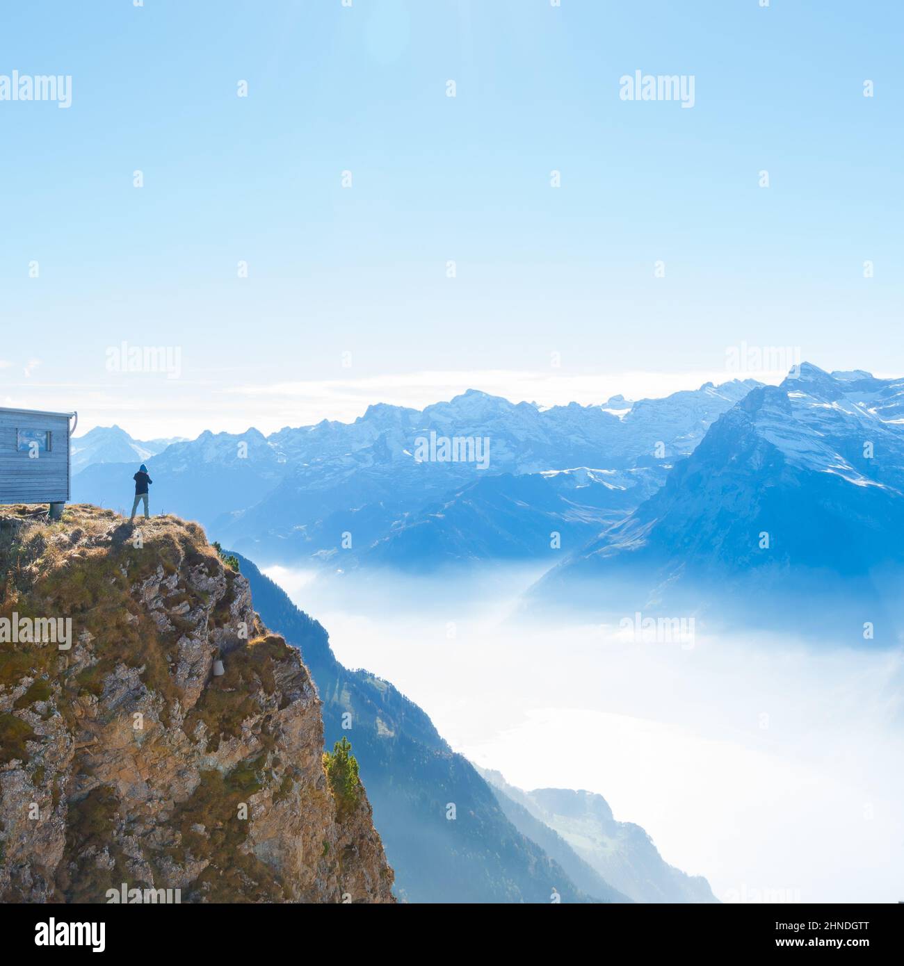 A male figure on top of a mountain. Grandiose panorama of mountains and clouds from the top. Stock Photo