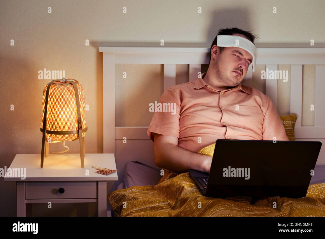 Adult sick man sleeping tiredly lying on bed with computer Stock Photo