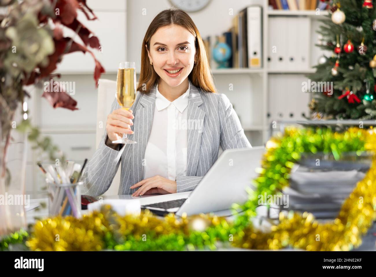 Business woman with a glass of champagne congratulates Merry Christmas on the Internet in office Stock Photo