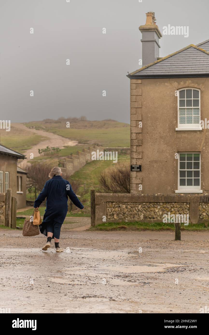 16th February, 2022. UK WEATHER - an elderly woman struggles returning to her seafront home as gale force winds pound Birling Gap East Sussex, UK Stock Photo