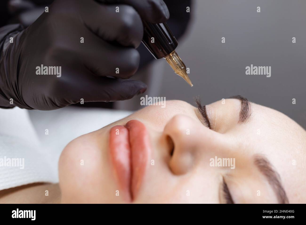 Close-up of a woman, in a beauty salon with her eyes closed, a cosmetologist makes permanent eyeliner makeup. Professional in black gloves and with a Stock Photo
