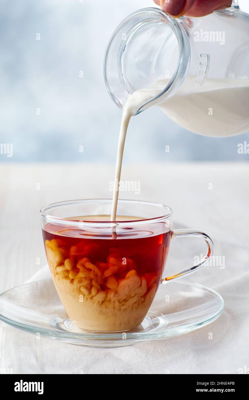 Pouring milk into cup of black tea on white wooden table Stock Photo