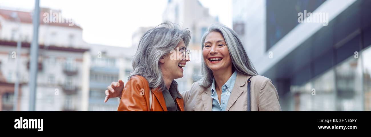 Beautiful grey haired women companions on modern city street at walking Stock Photo