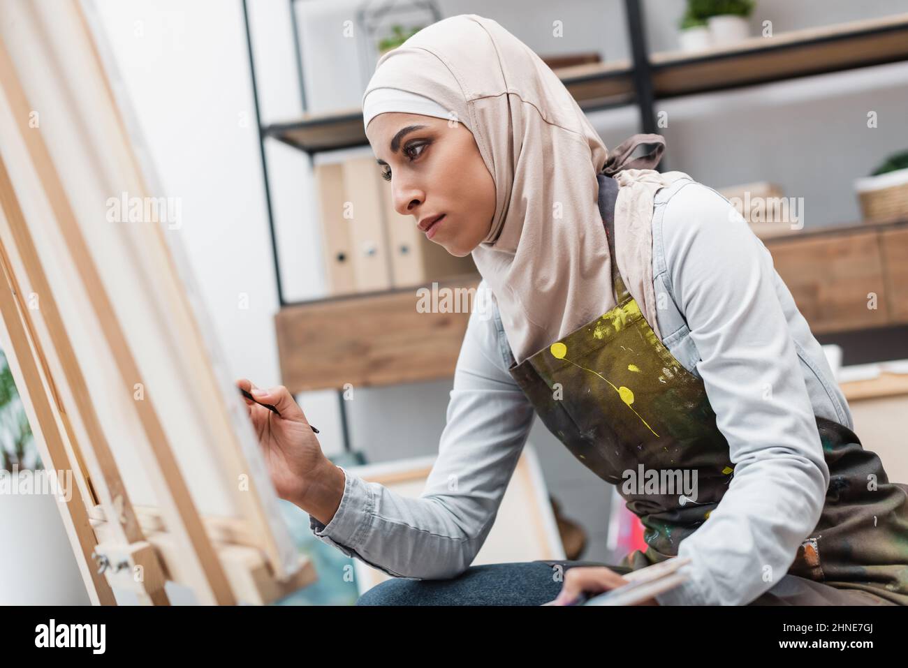 young arabian woman in hijab painting on blurred canvas at home Stock ...