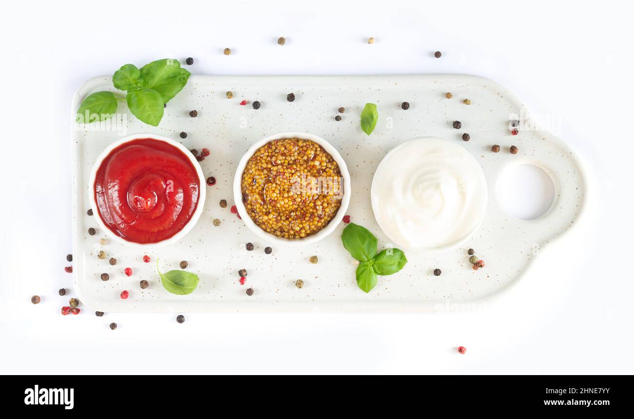 Set of popular sauces ketchup, dijon mustard and mayonnaise in small white bowls on ceramic