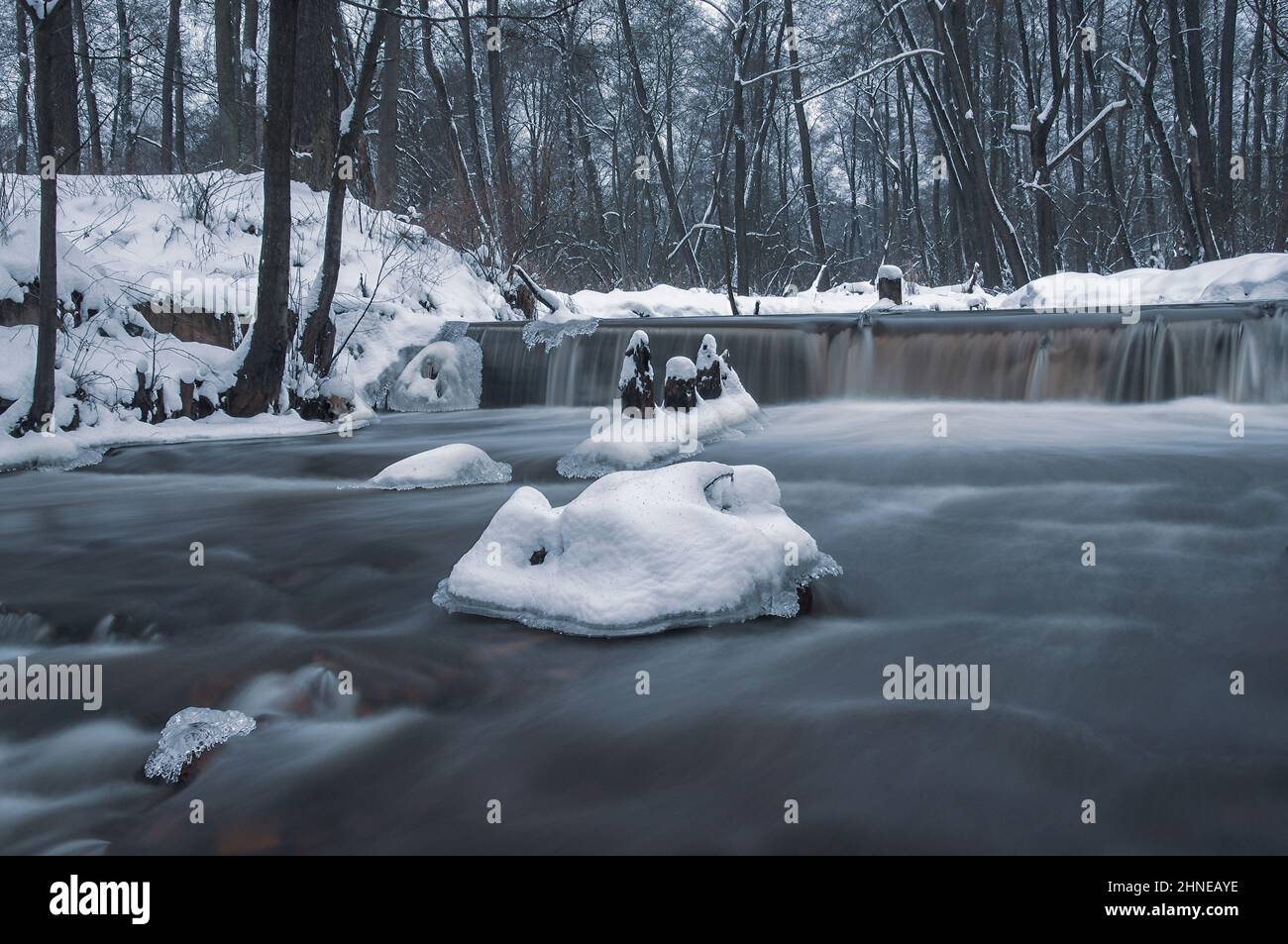 Waterfall on a small river in winter. There is snow on the shore, and some ice on the river. Stock Photo