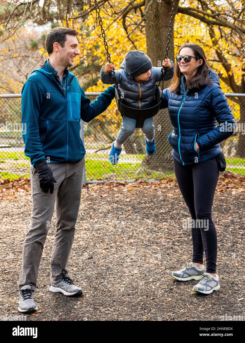 Young parents pushing two-year-old boy on a city playground swing; Philadelphia; Pennsylvania; USA Stock Photo