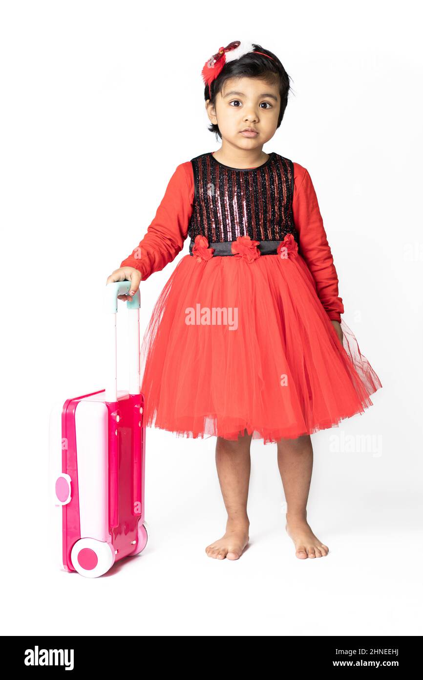Asian Indian Pretty Girl Kid In Red Dress Posing With Suitcase Luggage Bag On White Background. Fun, Travel, Tourist, Vacation, Holiday, Voyage, Trip, Stock Photo