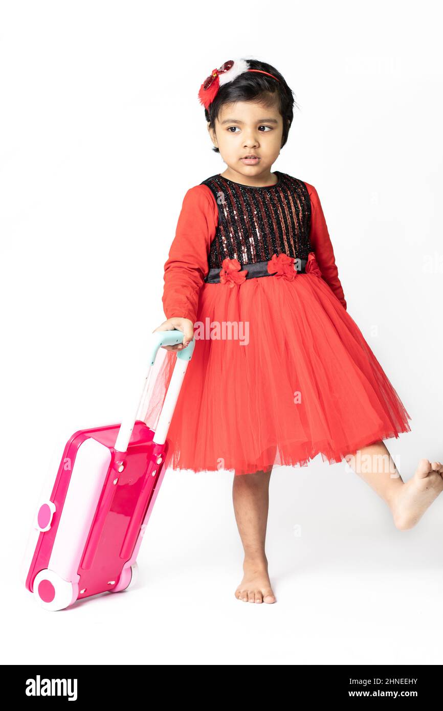 Asian Indian Pretty Girl Kid In Red Dress Posing With Suitcase Luggage Bag On White Background. Fun, Travel, Tourist, Vacation, Holiday, Voyage, Trip, Stock Photo