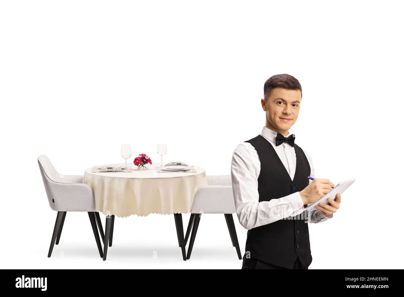 Young male waiter with a bow tie in front of a restaurant table isolated on white background Stock Photo