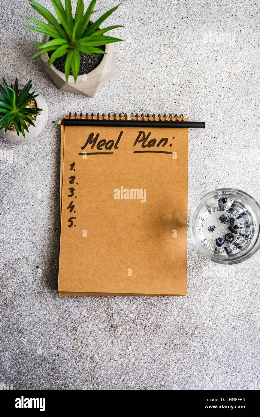 Notepad with Meal Plan list, glass of water and houseplants Stock Photo