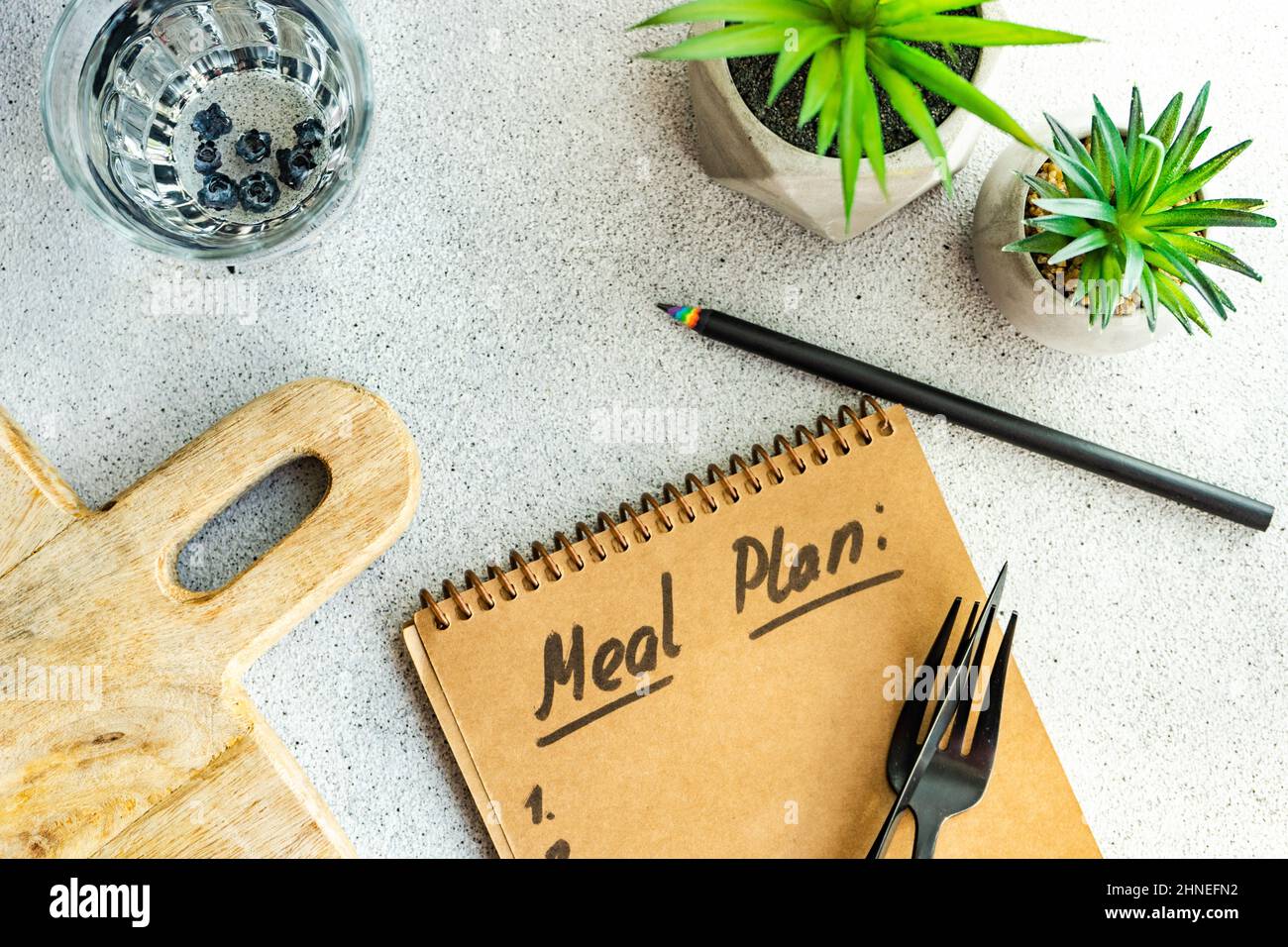 Glass of water, Meal plan Notepad, houseplants and a chopping board on a table Stock Photo