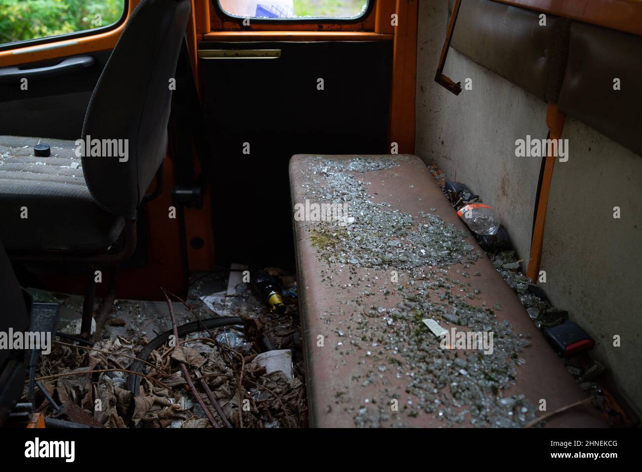 Broken glass on a rear bench seat of an old orange delivery van in front of an old abandoned sanatorium, Germany Stock Photo