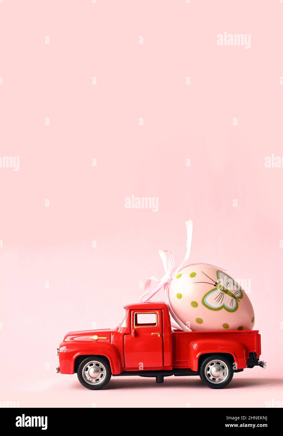 One Easter egg on a small car on a pink background. Copy space. Easter card. Stock Photo