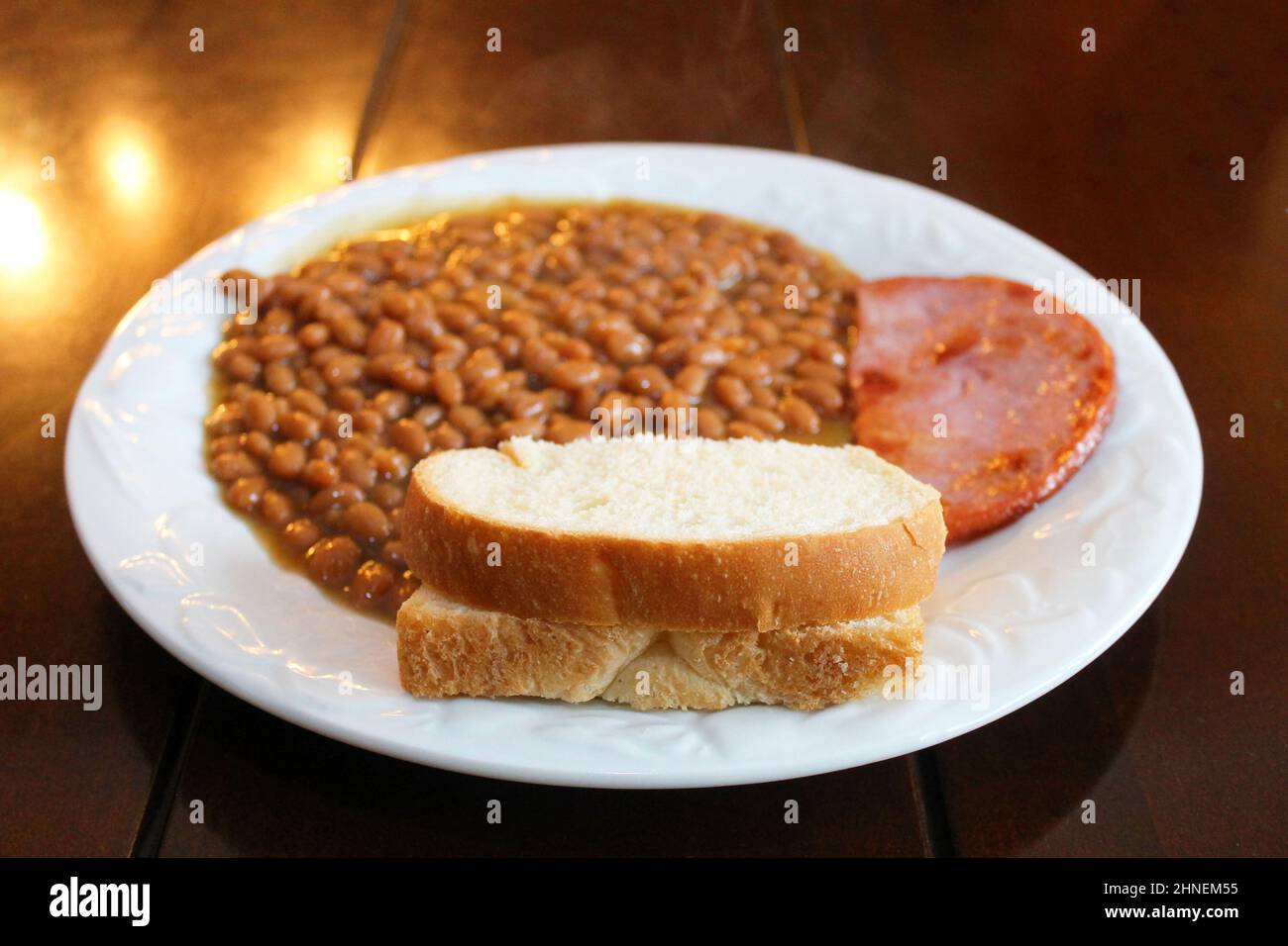 Close-up of a plate of baked beans with ham and a slice of bread. Stock Photo