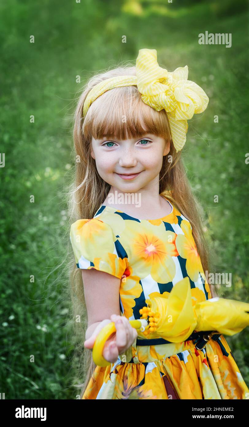 beautiful red-haired girl with yellow bow and yellow umbrella. An 11-year-old girl looks into the camera and smiles. Stock Photo