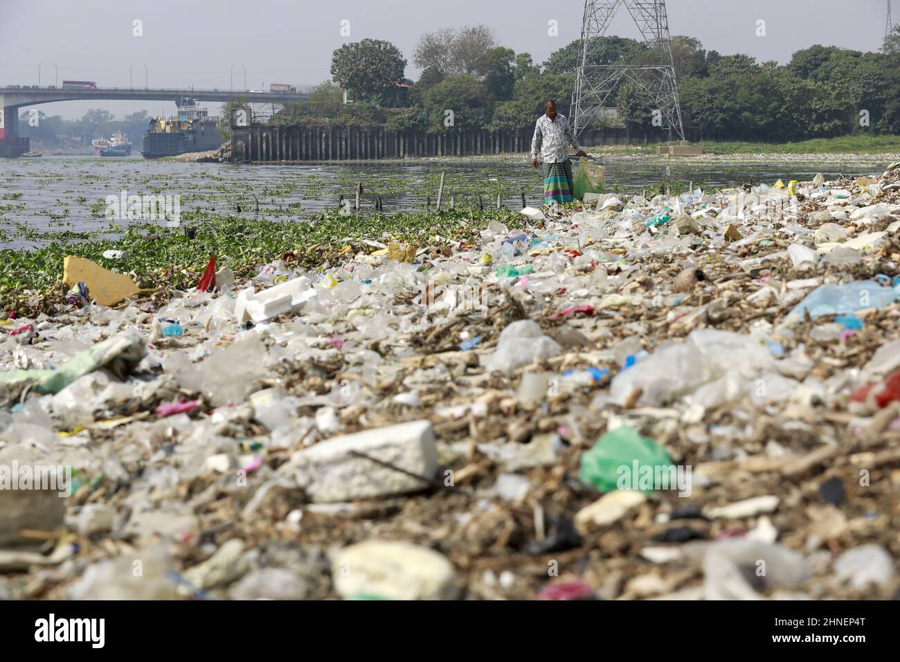 A man collects discarded plastic items on the banks of the river Buriganga, in Dhaka, Bangladesh, February 16, 2022. Industrial waste and sewage from the city are all dumped into the rivers. The once fresh and flowing rivers like Buriganga, is now submerged in pollution. The other rivers of the country face the same fate. Recent research has brought an even more horrendous picture into view. And that is plastic pollution. In just the four rivers that surround the capital city Dhaka, 30,000 tonnes of plastic waste were discovered. Half of this was in the river Buriganga. (Photo by Suvra Kanti D Stock Photo