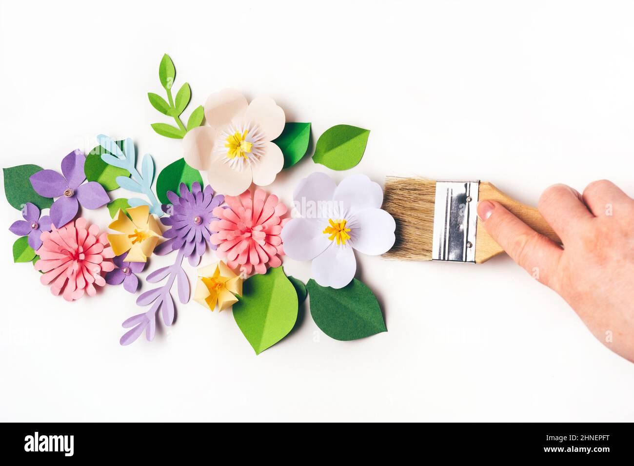 Womans hand holding brush in front of the paper flowers on white ...
