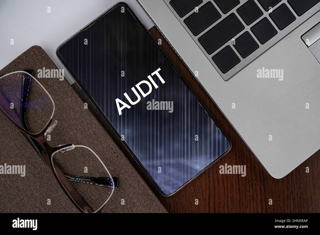 Top view of phone on table near laptop, notepad and glasses with inscription audit. Stock Photo
