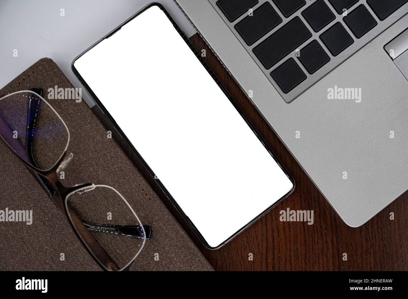 Top view of phone on table near laptop, notepad and glasses with white screen. Stock Photo
