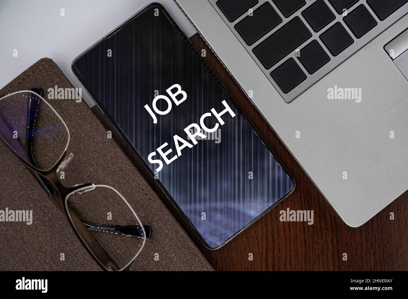 Top view of phone on table near laptop, notepad and glasses with inscription job search. Stock Photo