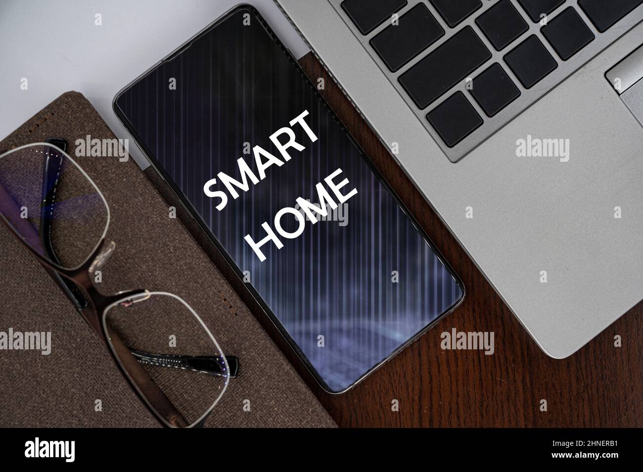 Top view of phone on table near laptop, notepad and glasses with inscription smart home. Stock Photo