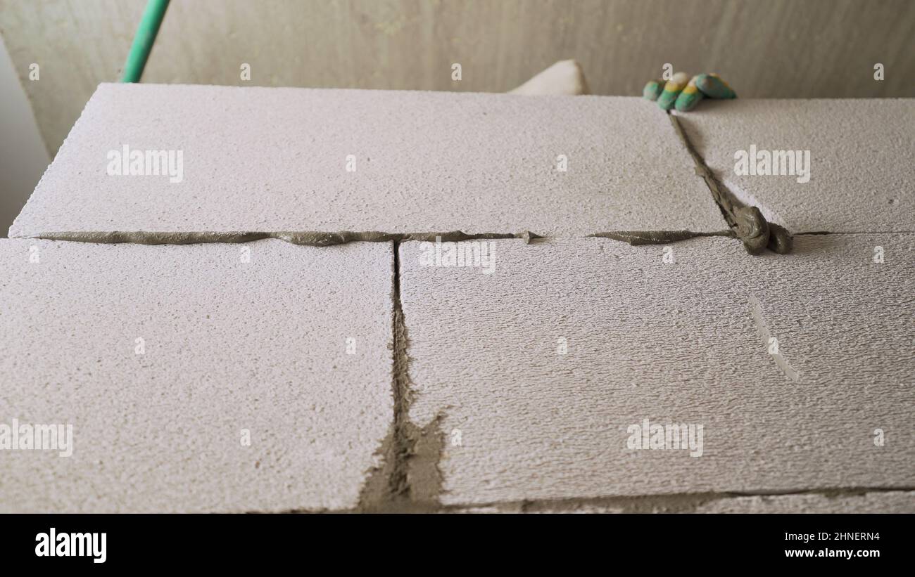 A worker erects a wall from a block. Bricklayer builder working with autoclaved aerated concrete blocks. Engineering and constructions concepts. Stock Photo