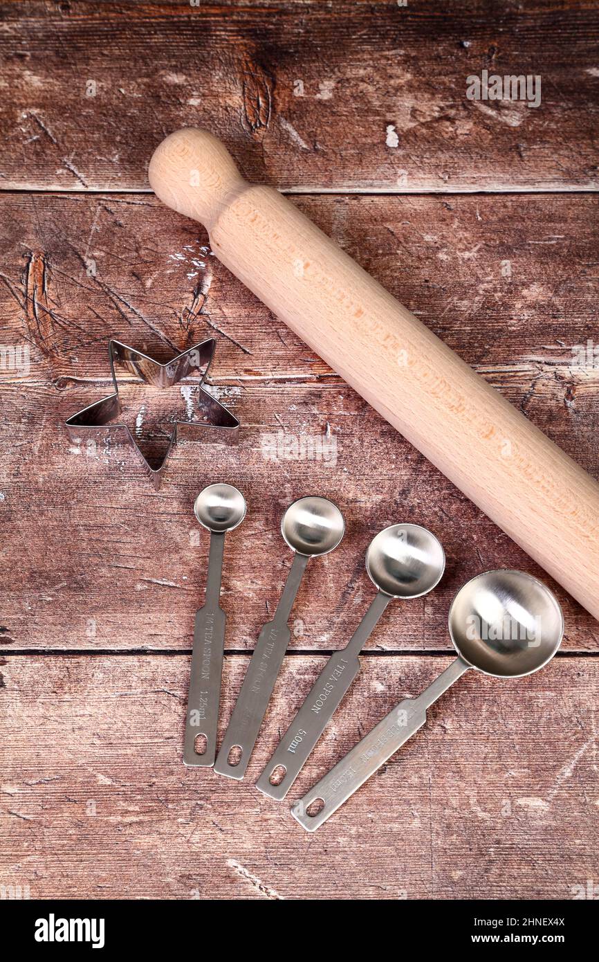 Wooden kitchen table with a set of stainless steel measuring spoons,rolling pin and pastry cutter, baking concept Stock Photo