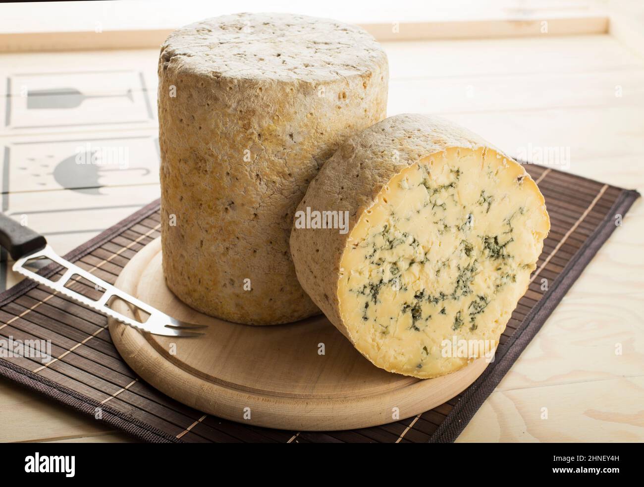 Cheddar PDO cheese with herbs cut and served on a wooden plate Stock Photo
