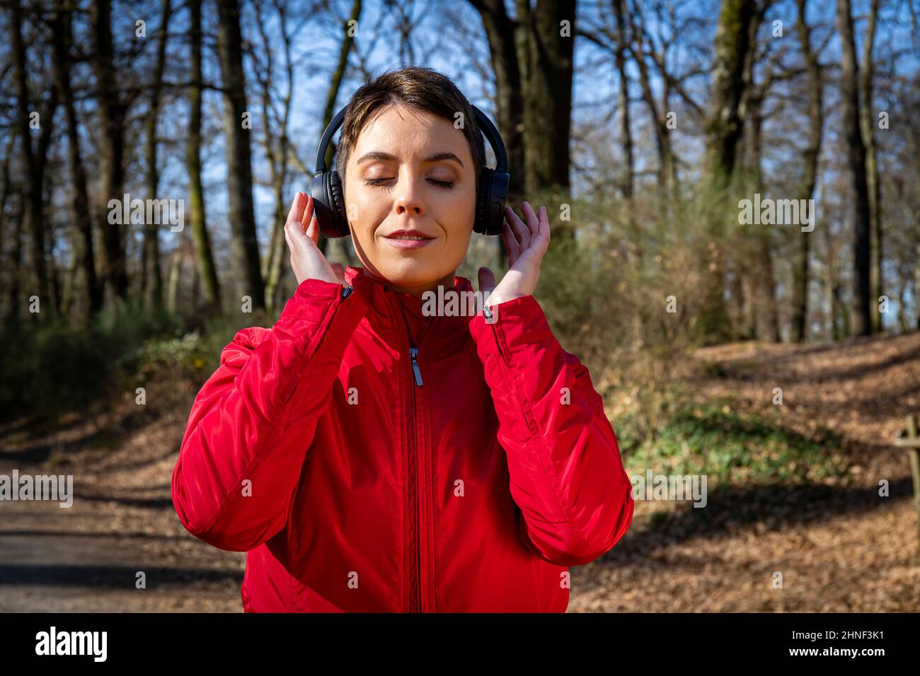 Young woman is training in the forest. Beautiful woman with short hair is listening to the music while she walks in the park. Stock Photo
