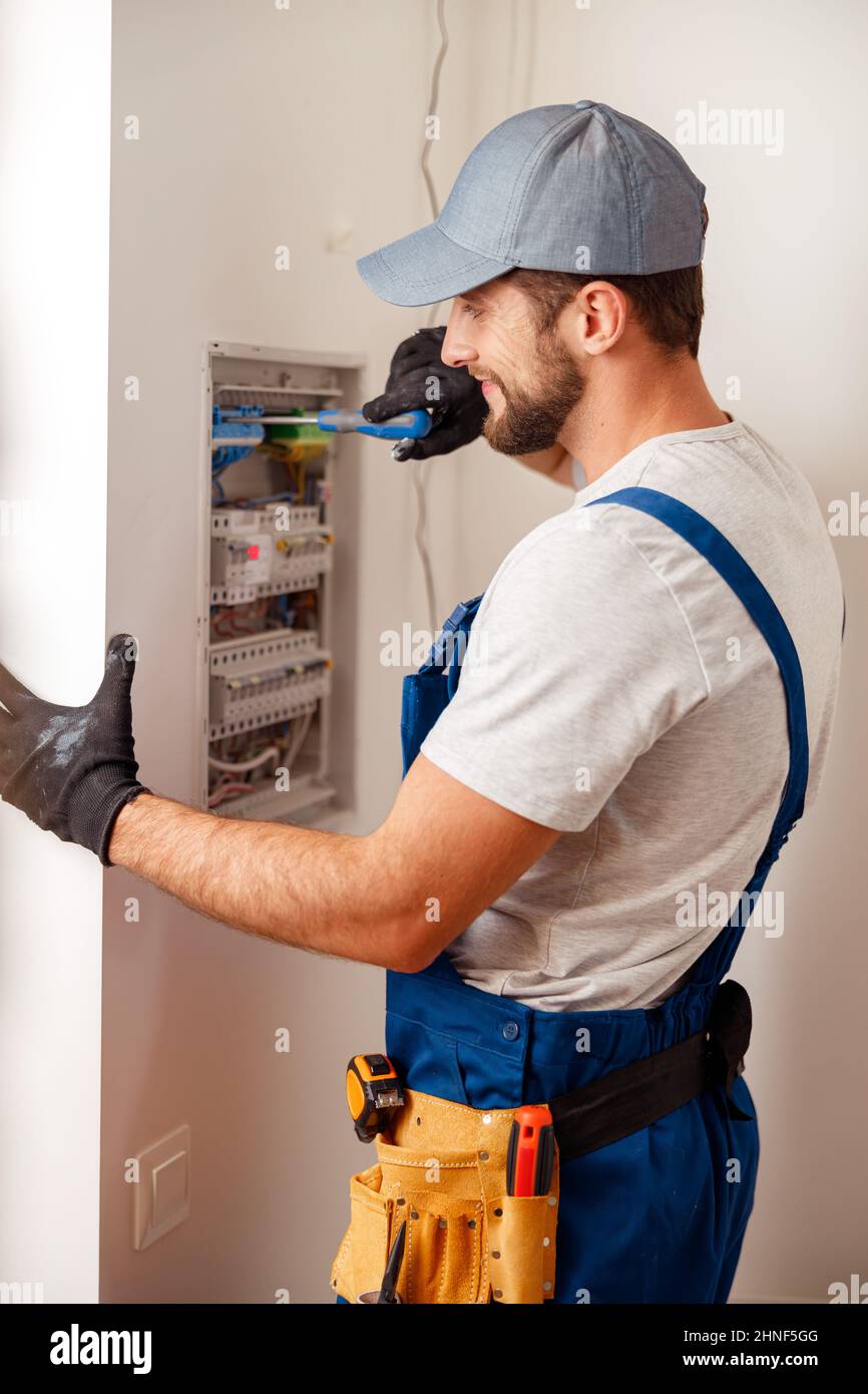 Electrical technician in uniform looking focused while checking fuses in a switchboard Stock Photo