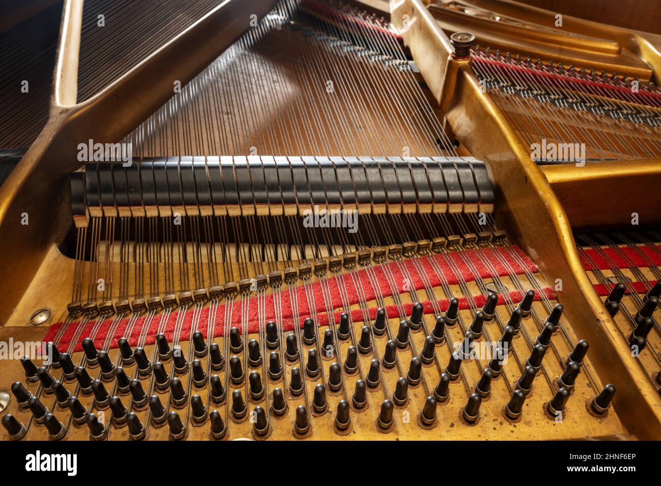 Inside an older grand piano with metal frame, strings, hammer, damper and red felt, mechanics of the acoustic musical instrument, music and culture co Stock Photo