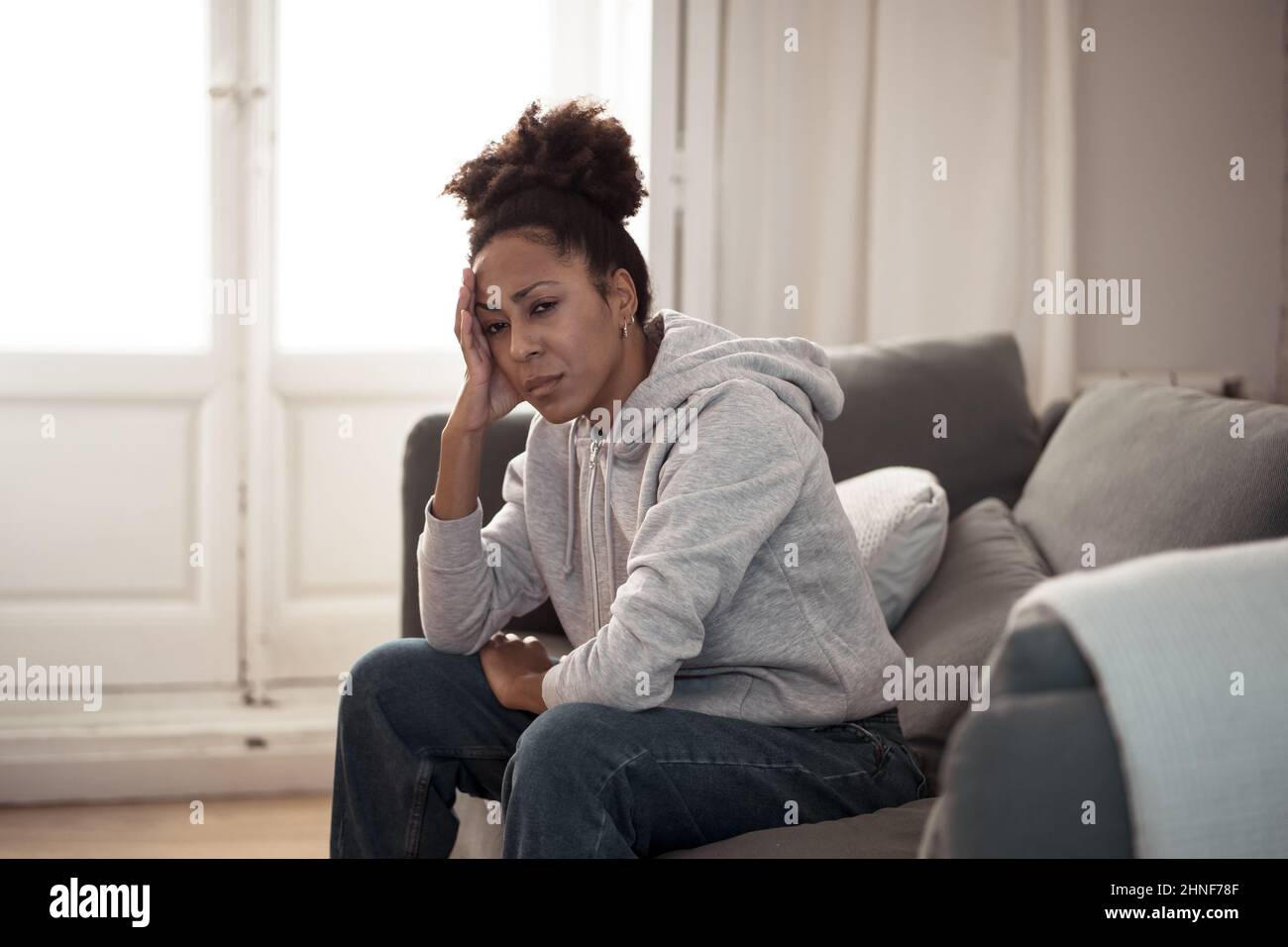 Depressed young attractive african american woman lying on sofa couch at home feeling sad tired and worried suffering depression stress and anxiety in Stock Photo
